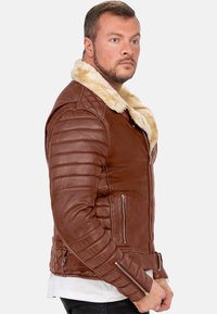 Giubbotto di pelle marrone con colletto in shearling crema, maniche trapuntate, doppi zip e tasche laterali. Vestibilità strutturata e texture liscia.