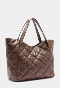 Smeđa torba od quilted kože s dva remena za rame, koja ima glatku teksturu i dijamantni uzorak za dodatnu detaljizaciju.