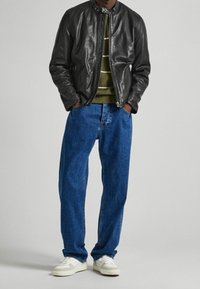 Giacca bomber in pelle nera, maglione a righe verdi, jeans blu a vestibilità ampia e sneakers bianche. Focus sulla texture e sui colori a contrasto.