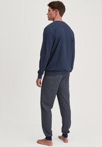 Marineblauwe sweatshirt met lange mouwen en ronde hals, gecombineerd met bijpassende joggers met een patroon in donkerblauw met golfachtige ontwerpen en elastische manchetten.