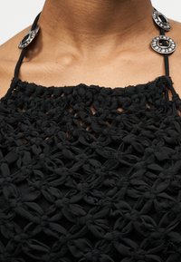 Μαύρο πλεκτό κορσέ με μεγάλα λουλουδένια σχέδια κόμπων και ασημένια διακοσμητικά κουμπιά στους ιμάντες γύρω από τον λαιμό.