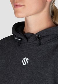Dunkelgrauer Kapuzenpullover mit Kordelzug, der ein weißes Logo auf der Brust hat. Die Stoffstruktur wirkt weich und glatt, mit einer bequemen Passform.