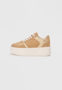 Baskets en suede beige avec des accents en cuir beige, à bout rond et avec des lacets plats. Elles ont une semelle plateforme blanche épaisse. Branding minimal visible.