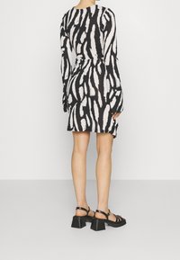 Černobíle vzorované šaty s dlouhými rukávy a přiléhavým střihem, doplněné černými masivními sandály na podpatku. Texturovaná tkanina.