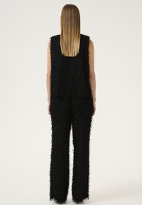 Ensemble noir texturé en deux pièces comprenant un haut sans manches et un pantalon ample, tous deux avec une apparence shaggy et des silhouettes droites.