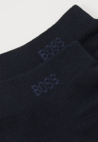 Mørkeblå sokker lavet af et blødt, tekstureret stof, med subtil "BOSS" branding i mørkere tråd langs ribbenen.