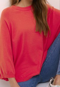 Fuchsia übergroßer Pullover, gestrickte Textur, gerippter Halsausschnitt und Bündchen, mit gesenkten Schulternähten, kombiniert mit blauen Jeans.