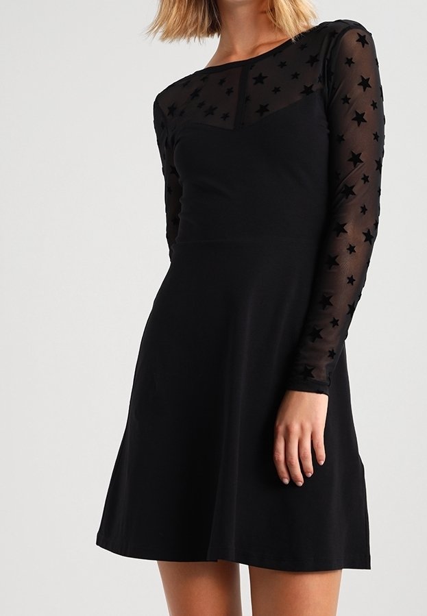 Czarna sukienka z dopasowanym gorsetem i rozkloszowanym dołem. Długie rękawy wykonane z przezroczystego materiału z wzorem gwiazd. Gładka tekstura, prosty design.