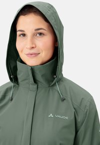 Grüne wasserdichte Jacke mit Kapuze, verstellbaren Kordelzügen und einer glatten Textur. Enthält ein helles Logo auf der Brust.