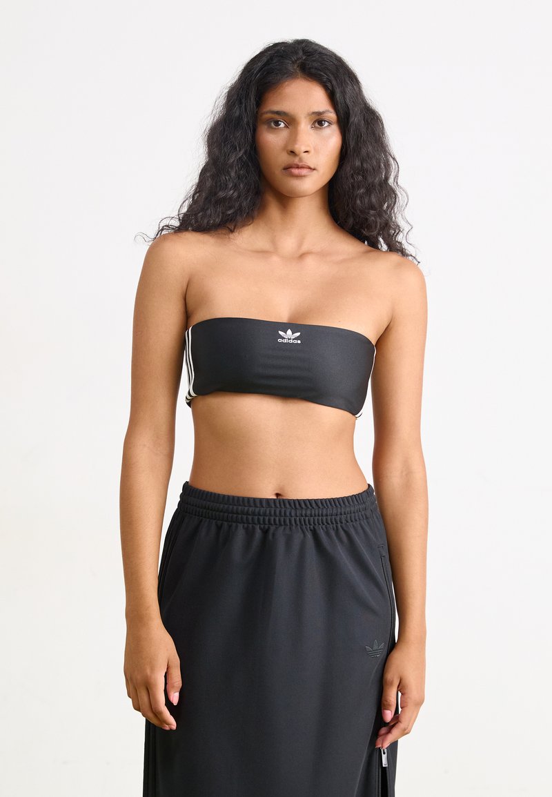 Top bandeau preto com logótipo Adidas branco e riscas laterais, combinado com uma saia preta de cintura alta com fecho éclair e tecido texturizado.
