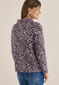 Sweter dzianinowy z wysokim kołnierzem, z fioletowo-białym geometrycznym wzorem. Miękka, teksturowana tkanina oraz luźne rękawy.