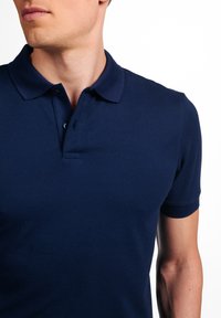 Marineblauwe polo met korte mouwen, voorzien van een klassieke kraag, knoopsluiting en textuurstof. Het heeft een getailleerd ontwerp dat het lichaam volgt.
