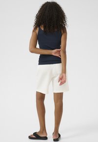 Marineblaues, geripptes Tanktop, weiße Shorts und schwarze Flip-Flops. Sichtbare Nahtdetails und lockere Passform, die ein lässiges Outfit von hinten zeigt.