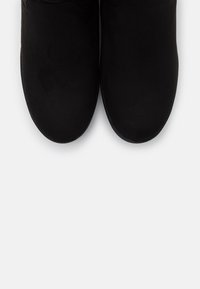 Bottines en daim noir avec une texture lisse, bout rond et semelle plate, vues de dessus. Design minimaliste sans embellissements.