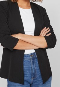 Svart öppet blazer med trekvartslånga ärmar, parat med en vit topp och högmidjade blå jeans; slät textur och skräddarsydd passform.