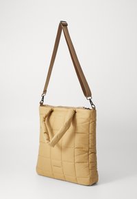 Quilted tote bag in light yellow with a textured finish, featuring dual handles and a detachable shoulder strap. Zippered top closure.