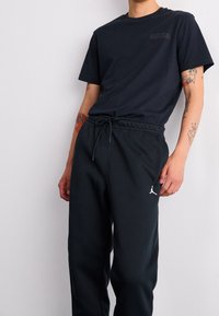Svart t-shirt med en liten logotyp på bröstet, kombinerad med mörka joggers som har en vit Jumpman-logotyp. Blandmaterial av bomull, avslappnad passform.