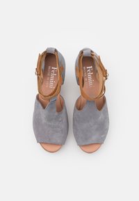 Sandales ouvertes en suède gris avec des accents en cuir brun. Lanière de cheville réglable et semelle plate. Présente des côtés exposés. Logo de la marque visible à l'intérieur.