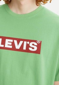 Zelené bavlněné tričko s velkým červeným obdélníkovým grafickým prvkem a bílým textem "LEVI'S®" na hrudi; krátké rukávy, kulatý výstřih.