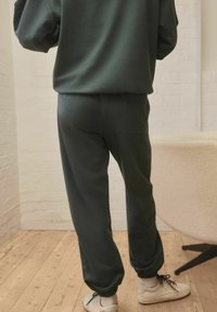 Rohelised joggers pehmest kangast, elastse vöökoha ja mansettidega, lõdva istuvusega ning tagaküljel nähtava küljetaskuga.