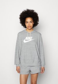 Felpa grigia Nike con un grande logo bianco e cordino regolabile, abbinata a pantaloni corti grigi coordinati con un piccolo logo sulla gamba.