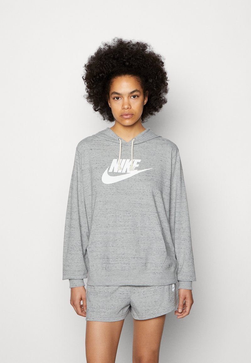 Felpa grigia Nike con un grande logo bianco e cordino regolabile, abbinata a pantaloni corti grigi coordinati con un piccolo logo sulla gamba.