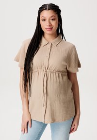 Helles beige Kurzarmhemd aus strukturiertem Stoff, mit knöpflingem Vorderteil und gerafftem Taillendesign, kombiniert mit hellblauen Jeans.