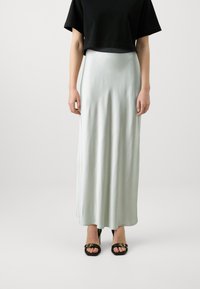 Lys grøn satin maxi skjørt med en glatt tekstur, sideslitt detalj, sammen med en svart kort t-skjorte og svarte sandaler med åpen tå.