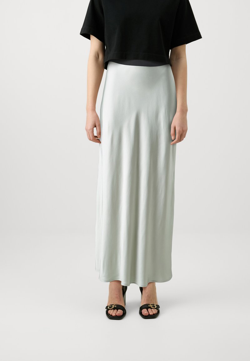 Lichtgroene satijnen maxi-jurk met een gladde textuur, met een zijspleet, gecombineerd met een zwart crop-top en zwarte sandalen met open tenen.