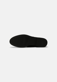 Semelle de chaussure noire avec un motif de grip texturé, des bords lisses et un bout arrondi. Présente une construction robuste avec des détails minimalistes.