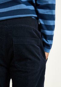 Marineblå cordfløjlsbukser med en tekstureret overflade, der har sidelommer og elastisk talje, parret med en blåstribet skjorte med lange ærmer.