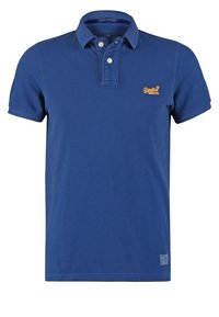 Blå polo skjorta i bomull, med en treknappslåning, klassisk krage och liten gul logotyp på br östet. Korta ärmar.