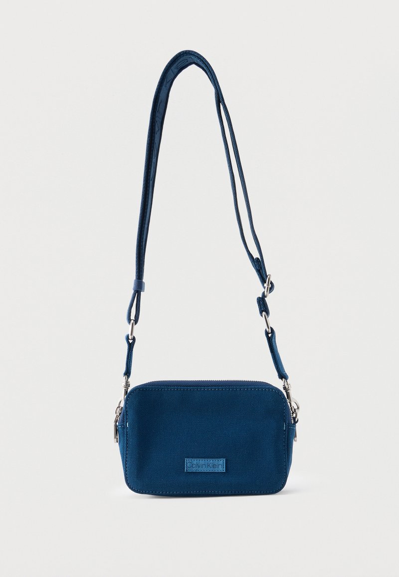 Μικρή ορθογώνια τσάντα ώμου σε ναυτικό μπλε με ρυθμιζόμενο λουράκι και ετικέτα μπροστά που εμφανίζει το λογότυπο Calvin Klein.