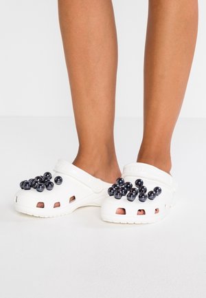 Sabots en plastique blancs présentant un design texturé, des trous de ventilation et des accents sphériques noirs sur la surface supérieure.