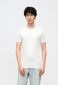 Wit t-shirt met korte mouwen van zacht katoen, met een ronde hals en een strakke pasvorm, gecombineerd met lichtblauwe spijkerbroek.