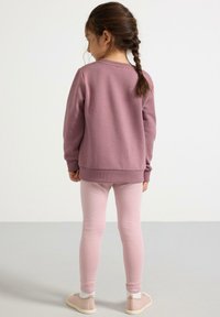 Vaatteet, joissa on violetti huppari, jonka hihansuissa ja helmassa on resorit, sekä tiukat vaaleanpunaiset leggingit. Lapsella on jalassaan vaaleat tennarit ja valkoiset nilkkasukat.