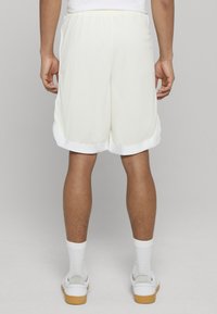 Bílé sportovní šortky s elastickým pasem a kontrastním bílým lemem, nošené s bílými ponožkami a teniskami.