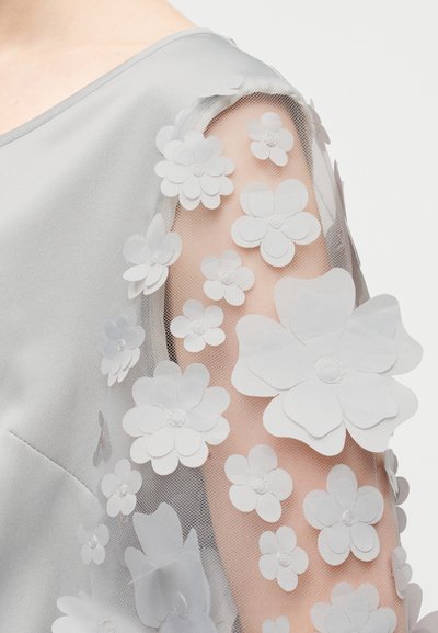 Γκρι φόρεμα με διαφανές μανίκι διακοσμημένο με λευκά υφασμάτινα λουλούδια και κέντρα από χάντρες. Λεπτό ύφασμα με ανθισμένες λεπτομέρειες.
