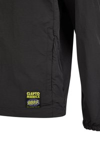 Schwarze wetterfeste Jacke mit einer seitlichen Reißverschlusstasche, elastischen Bündchen und einem auffälligen, bunten "CLEPTO MANICX" Logo-Patch.