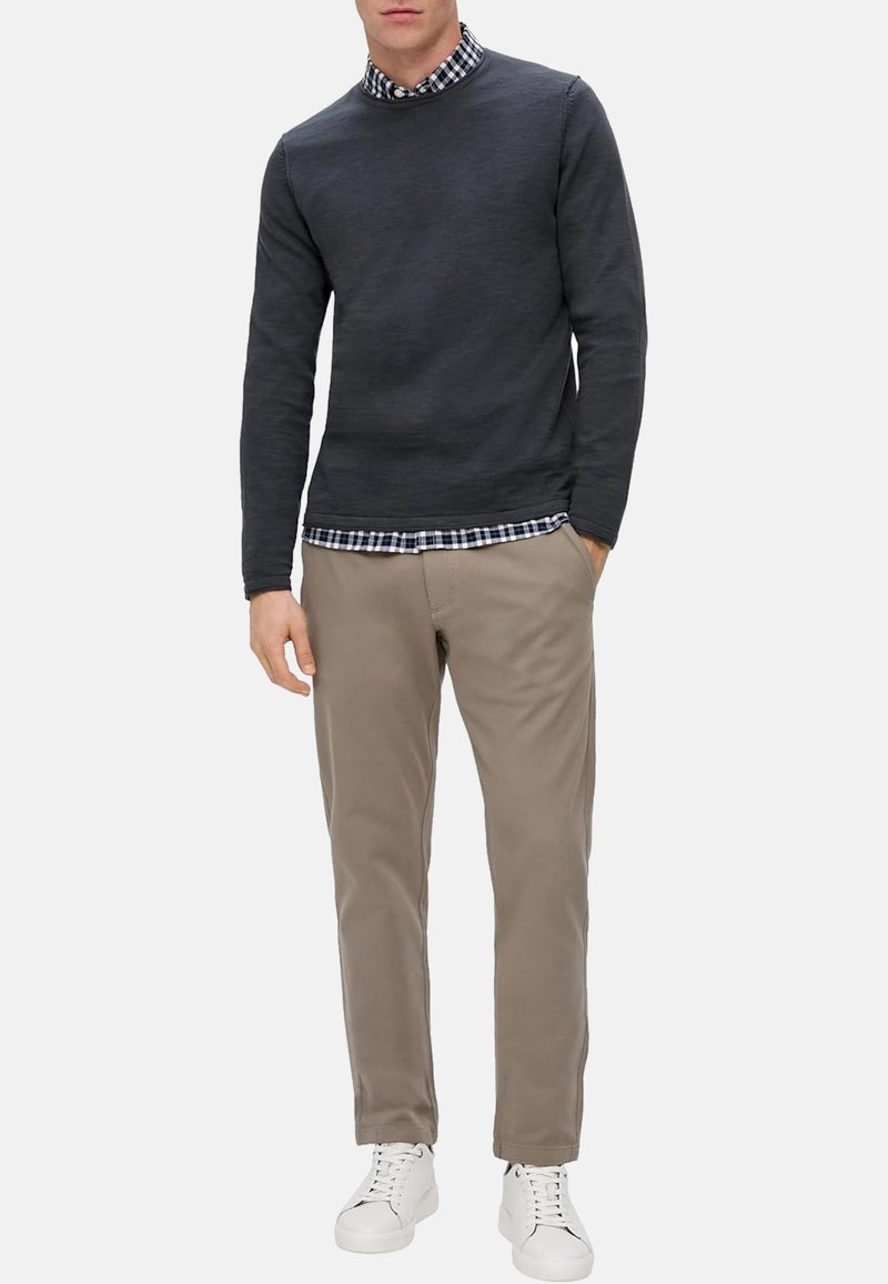 Donkergrijze trui met ronde hals over een blauw geruit button-up shirt, gecombineerd met beige chino's en witte sneakers. Casual outfit.