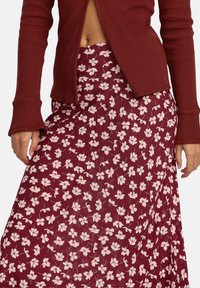 Haut côtelé bordeaux à manches longues, associé à une jupe longue avec un motif floral blanc sur fond bordeaux.