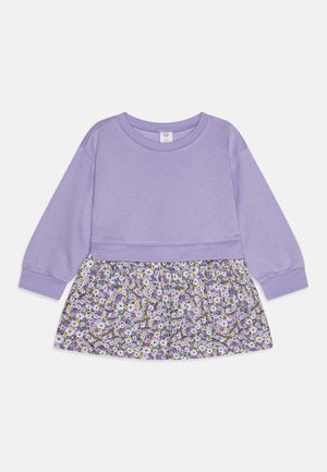 Maglione lilla con maniche lunghe, abbinato a una gonna a fiori nei colori viola, giallo e bianco. Tessuto morbido, design casual.