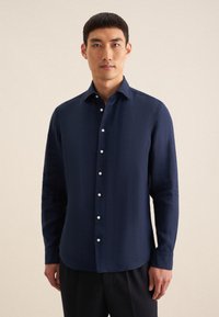 Marineblauwe blouse met lange mouwen, gemaakt van gladde stof, heeft een puntige kraag en een knoopsluiting met witte knopen, een getailleerde pasvorm en een afgeronde zoom.