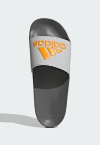 Gray slide sandal with a textured strap featuring an orange embossed logo. Smooth, dark gray footbed with a rounded toe design.