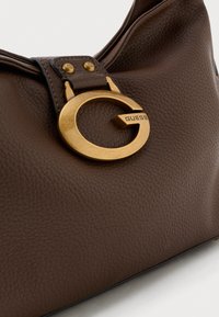 Bruine leren handtas met een opvallend gouden rond logo accent en een gestructureerd oppervlak met een slouchy ontwerp.
