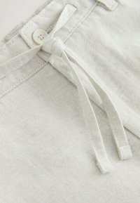 Pantalon beige clair avec un cordon en tissu noué en nœud et un bouton cousu près de la ceinture en gros plan.