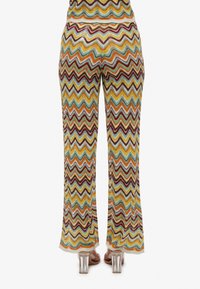 Pantalons en tricot colorés avec un motif en zigzag en jaune, teal, rouge et marron. Conception à jambes évasées avec une taille élastique et une texture transparente.