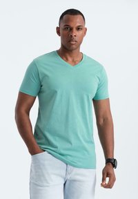 T-shirt in cotone verde menta con scollatura a V, maniche corte e vestibilità ampia, abbinato a jeans in denim blu chiaro.