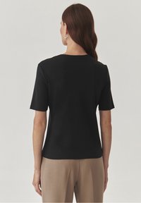 Schwarzes T-Shirt mit kurzen Ärmeln und rundem Ausschnitt, glatter Textur und lässigem Schnitt, kombiniert mit hellbraunen Hosen.