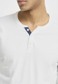 Fehér pamut henley ing, kerek nyakkivágással és sötétkék gombos záródással. Puha tapintású, testhezálló fazon.